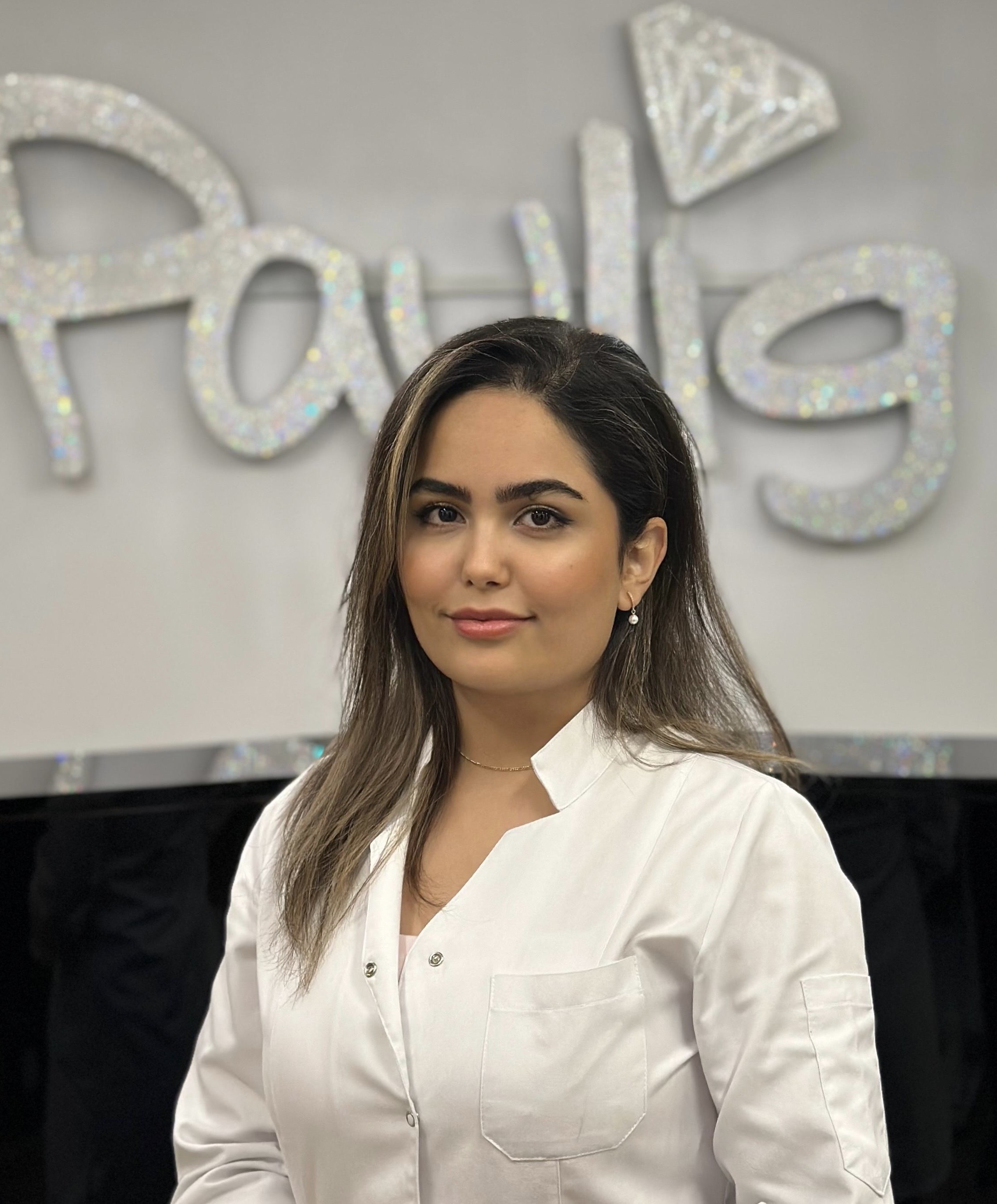 Frau mit langem Haar, neutraler Ausdruck, weißer Kittel, Hintergrund mit glitzerndem Logo.