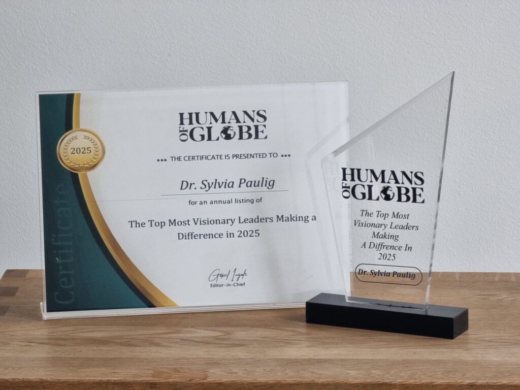 Zwei Auszeichnungen für Dr. Sylvia Paulig, eine Trophäe und ein Zertifikat, auf einem Holzregal.